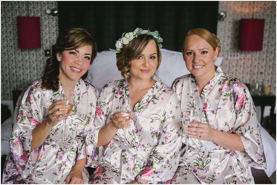 Bride in flower crown with her Bridesmaids wearing floral robes, at Hampton Manor wedding