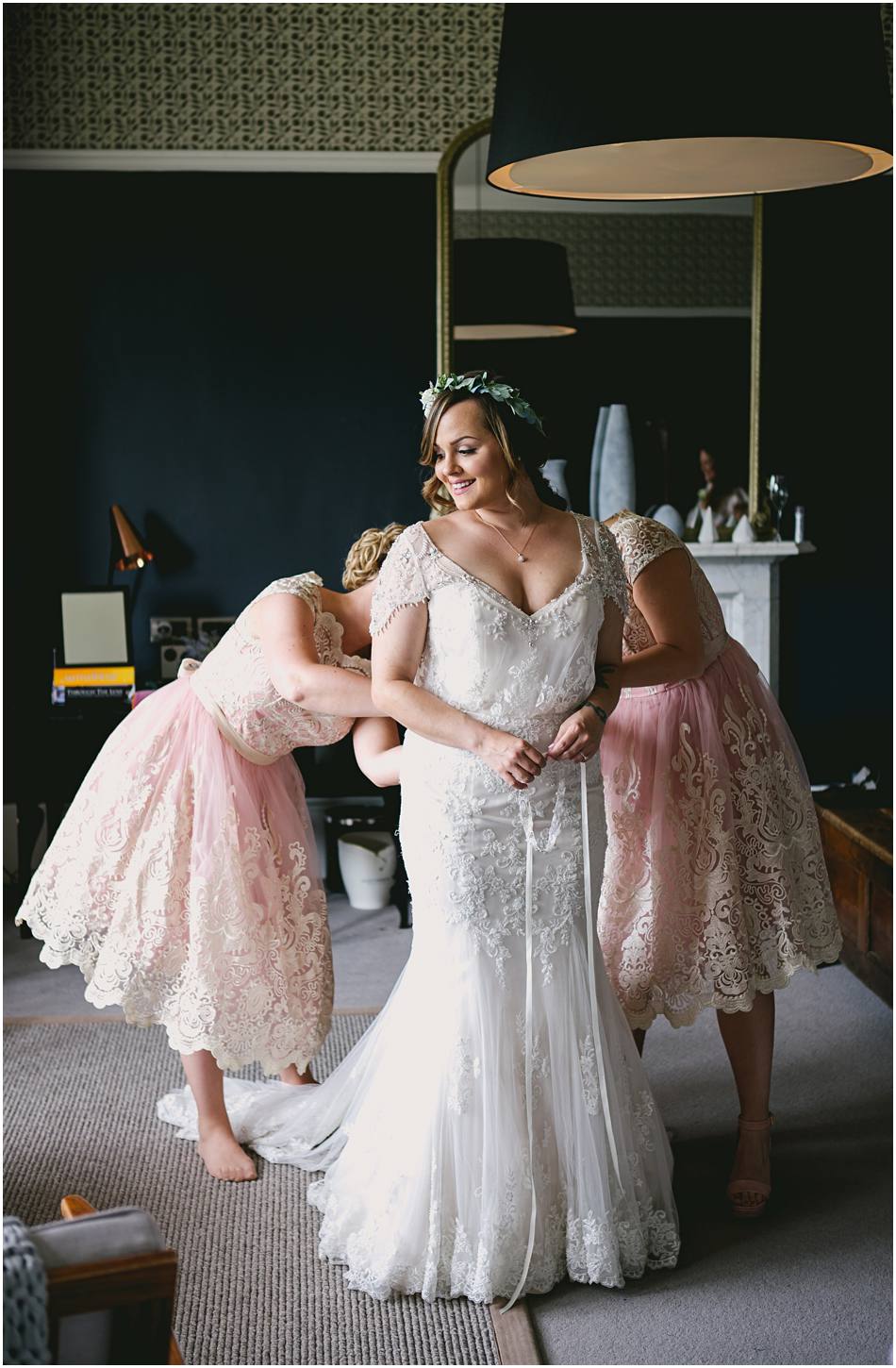 Bridesmaids in short pink lace dresses helping the Bride get ready on her wedding day