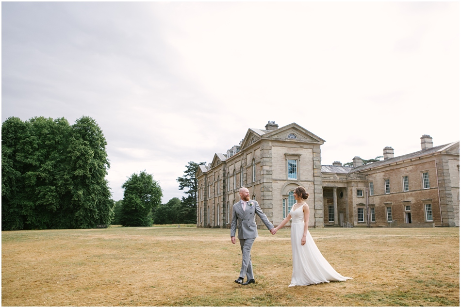 Compton Verney wedding photography; Bride and Groom walk holding hands with the house in the background