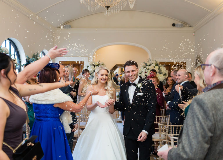 Bride and Groom walk down the aisle to confetti in the orangery at Alrewas Hayes. Groom wearing black tie