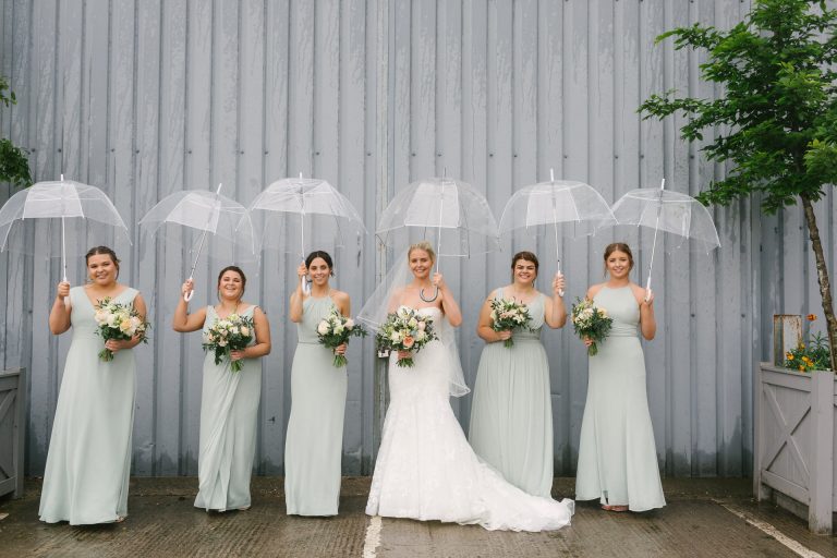 Bride and Bridesmaids wearing sage green dresses holding clear umbrellas