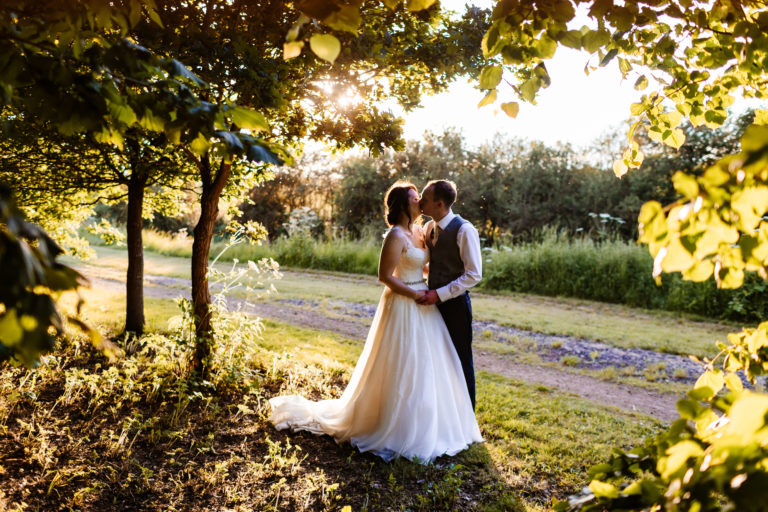 Groom wearing a waistcoat, shares a kiss with his Bride during golden hour in the grounds of Alrewas Hayes