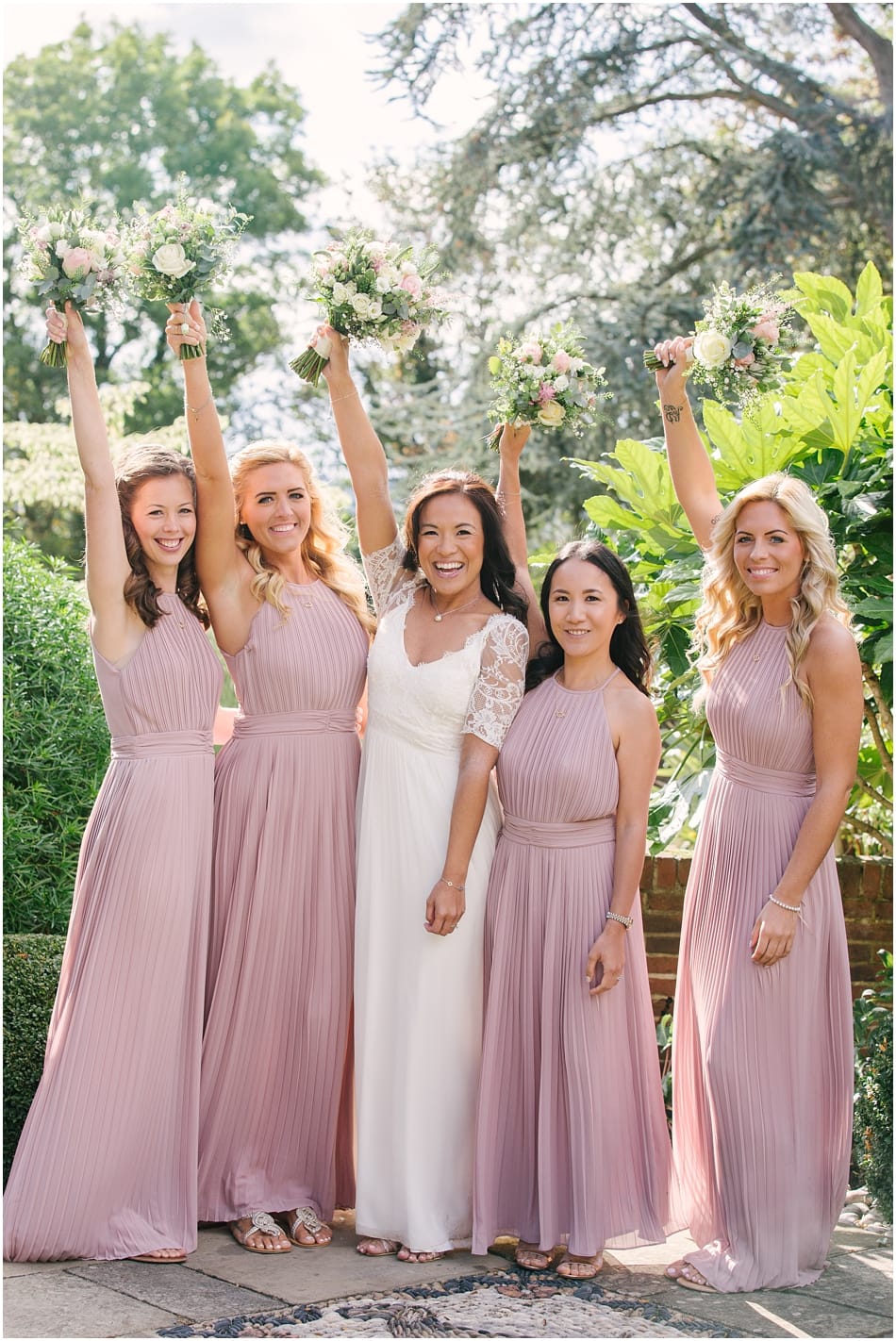 Bride and Bridesmaids wearing pink dresses with bouquets in the air at Gorcott Hall