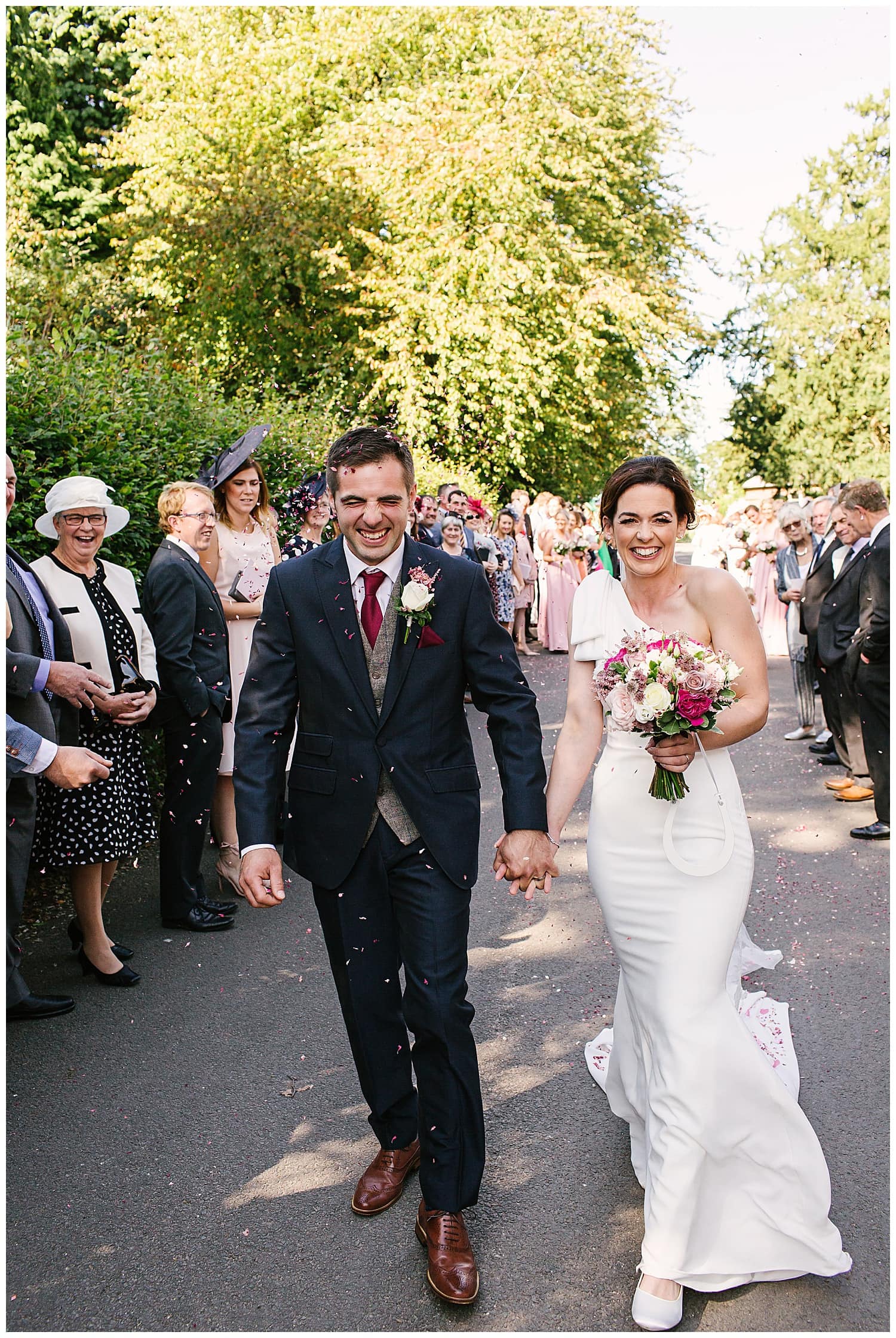 Newly married couple walking through confetti outside Ingestre Church, near Stafford