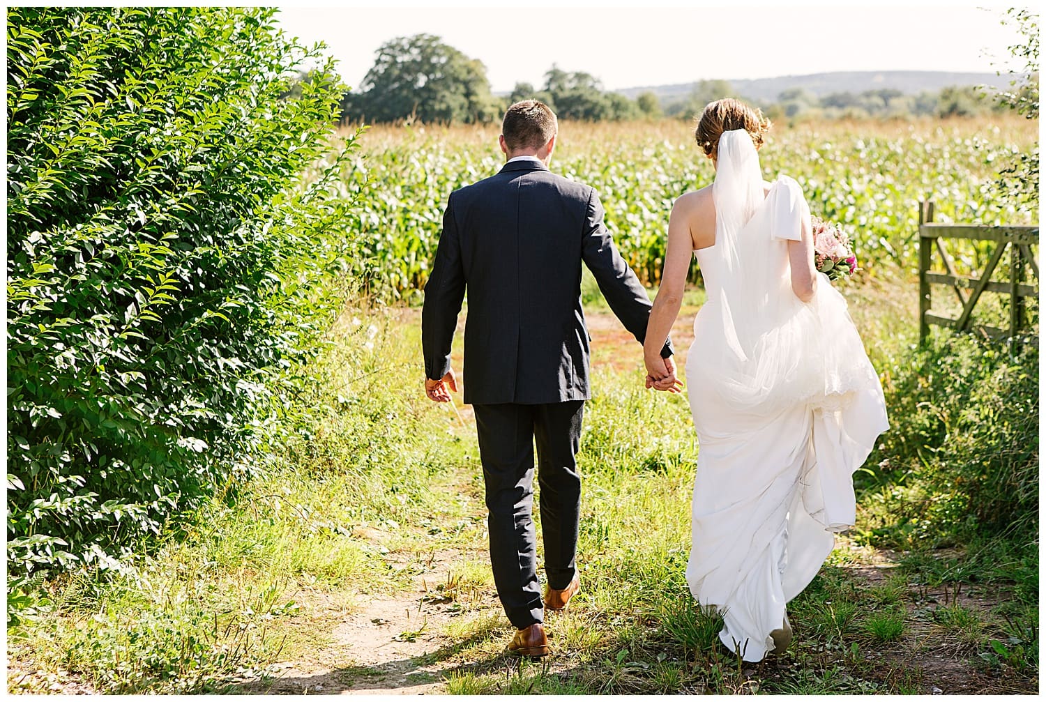 Newly married couple holding hands walk into cob field in rural Staffordshire