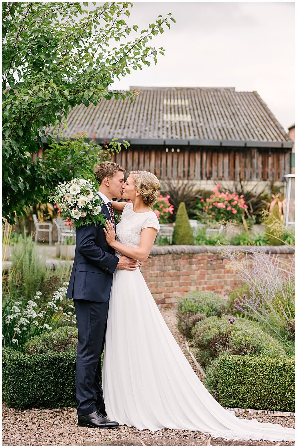 newly married couple kiss in front of a barn after their small wedding 