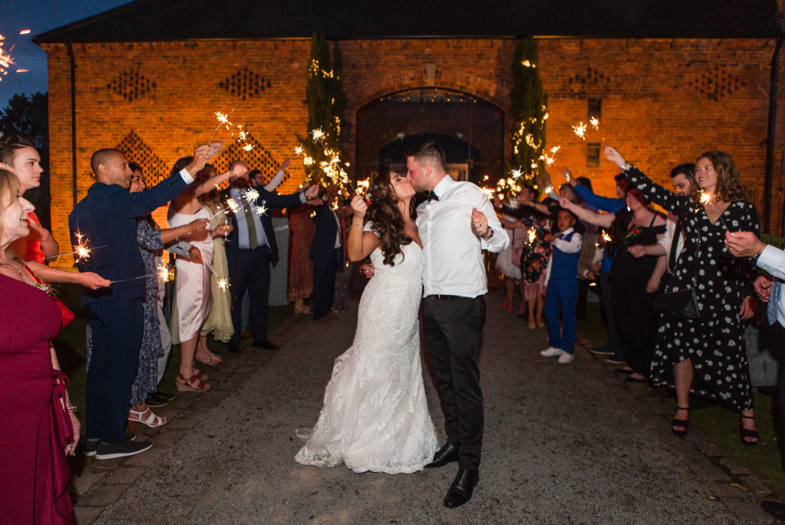 Bride and Groom kiss in front of their guests holding sparklers at night