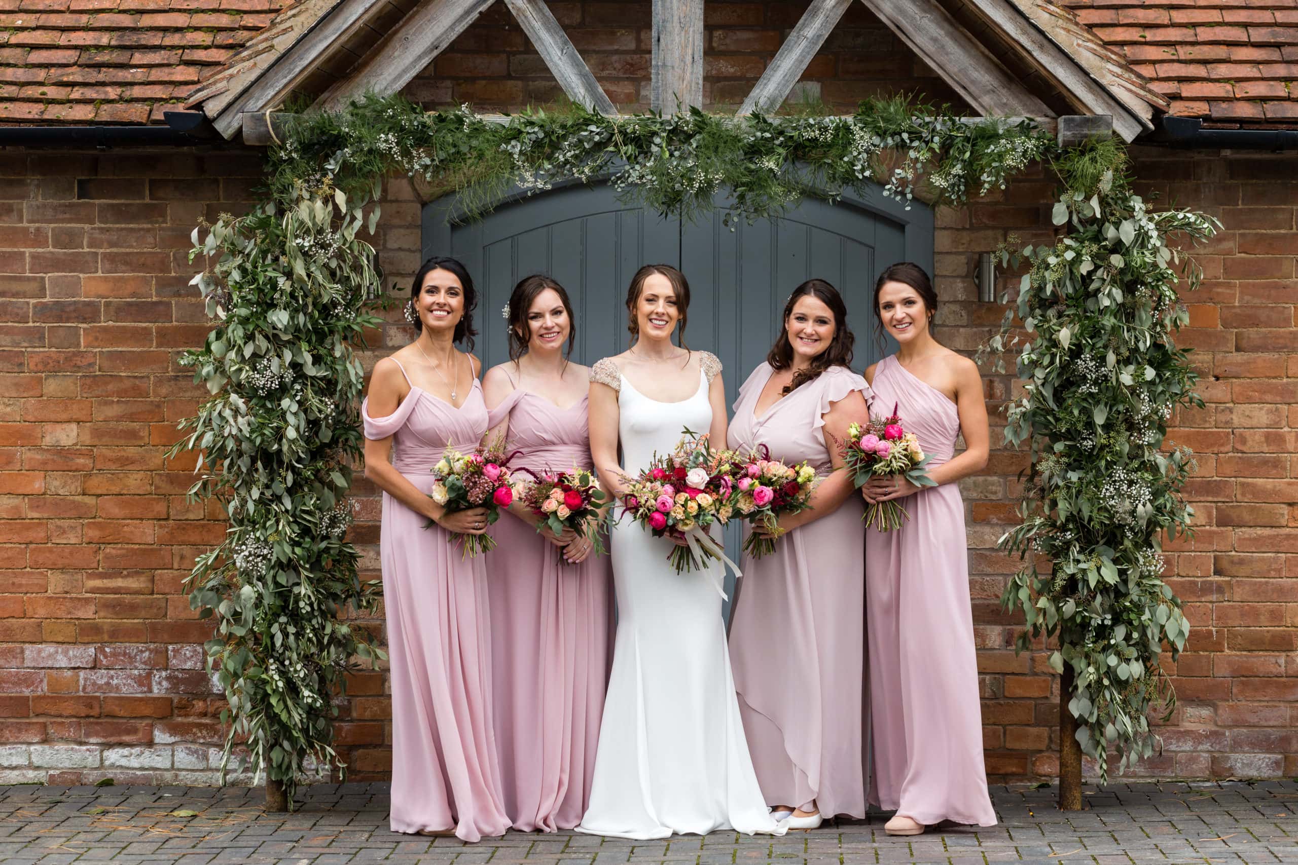 Bride stands with four bridesmaids wearing blush pink in front of grey door