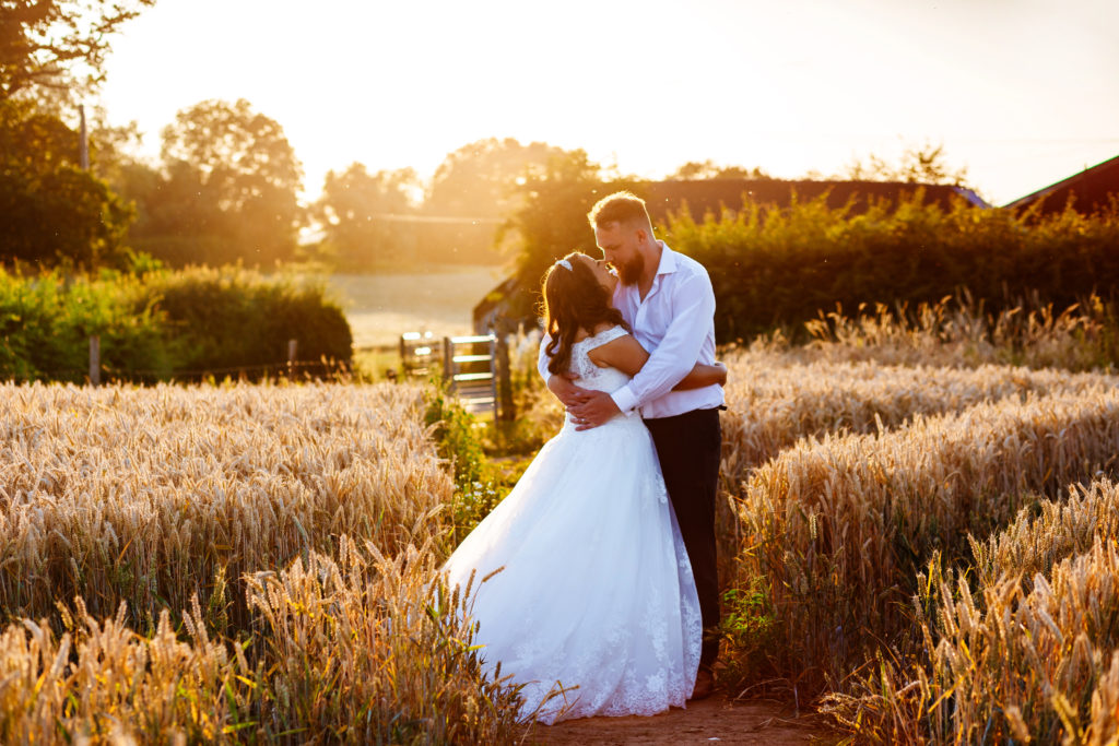 Curradine Barns wedding photography; Bride and Groom kissing at sunset in cornfields 