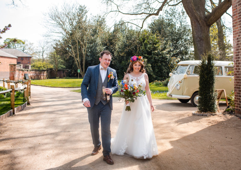 Bride and Groom walking in front of a cream VW Camper Van at their Thorpe Garden wedding