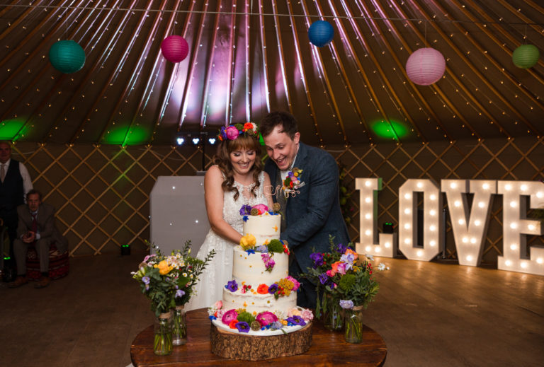 Bride and Groom cutting their wedding cake in the yurt at Thorpe Garden