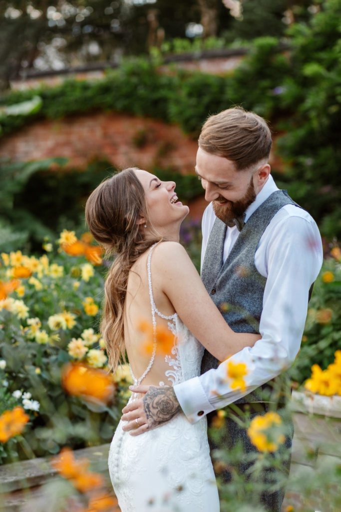 Thorpe Garden wedding photographer; natural photo of Bride and Groom laughing together with colourful flower beds