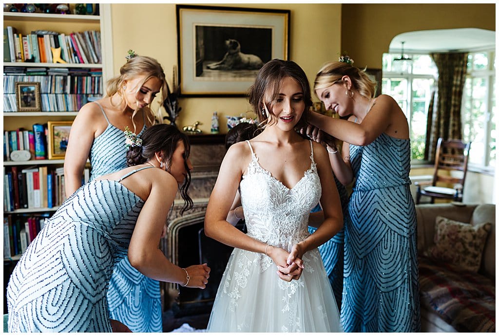 Bridesmaids in grey beaded dresses help dress the bride