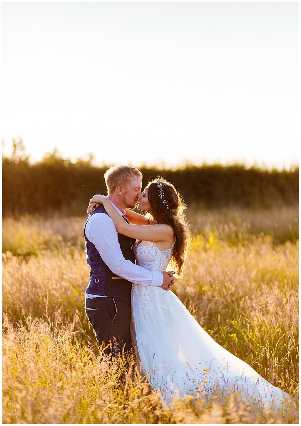 Groom wearing waistcoat kissing his Bride at sunset in a field in the village of Smallwood