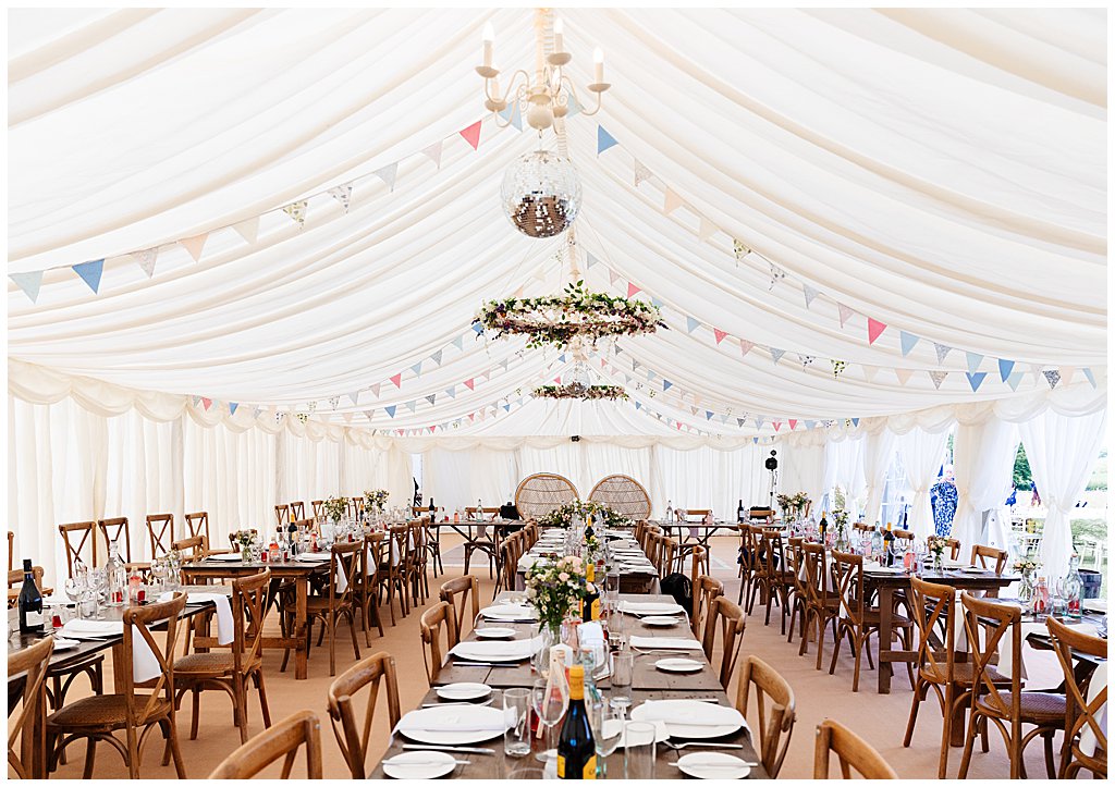 marquee wedding reception with wooden trestle tables and cane balloon back chairs