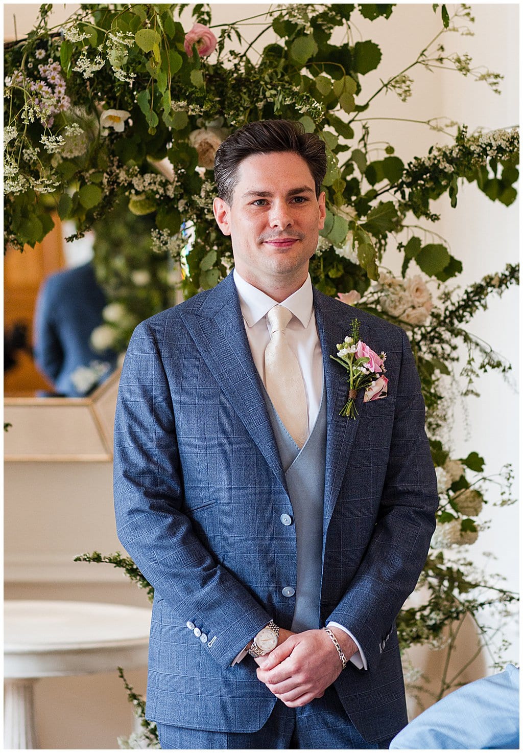 Groom stands in front of floral arch waiting for his bride