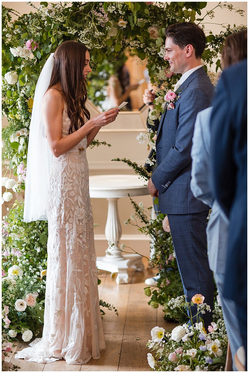 Bride reading personal vows to her Groom in front of a flower archway