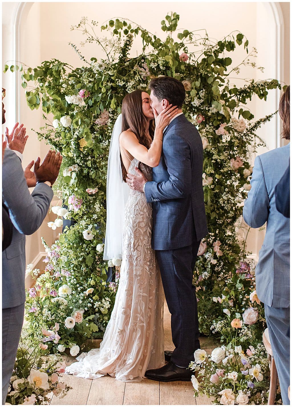 Bride and Groom first kiss in front of a large flower arch at Alrewas Hayes wedding venue