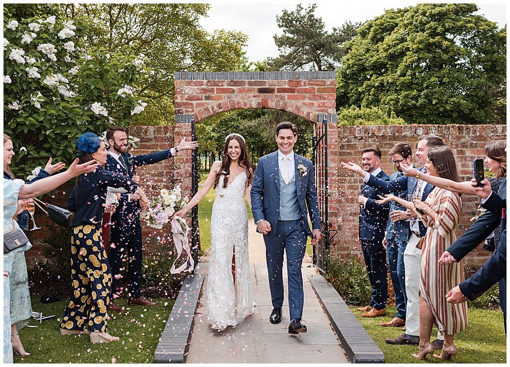 Bride and Groom smiling walking through confetti at Alrewas Hayes