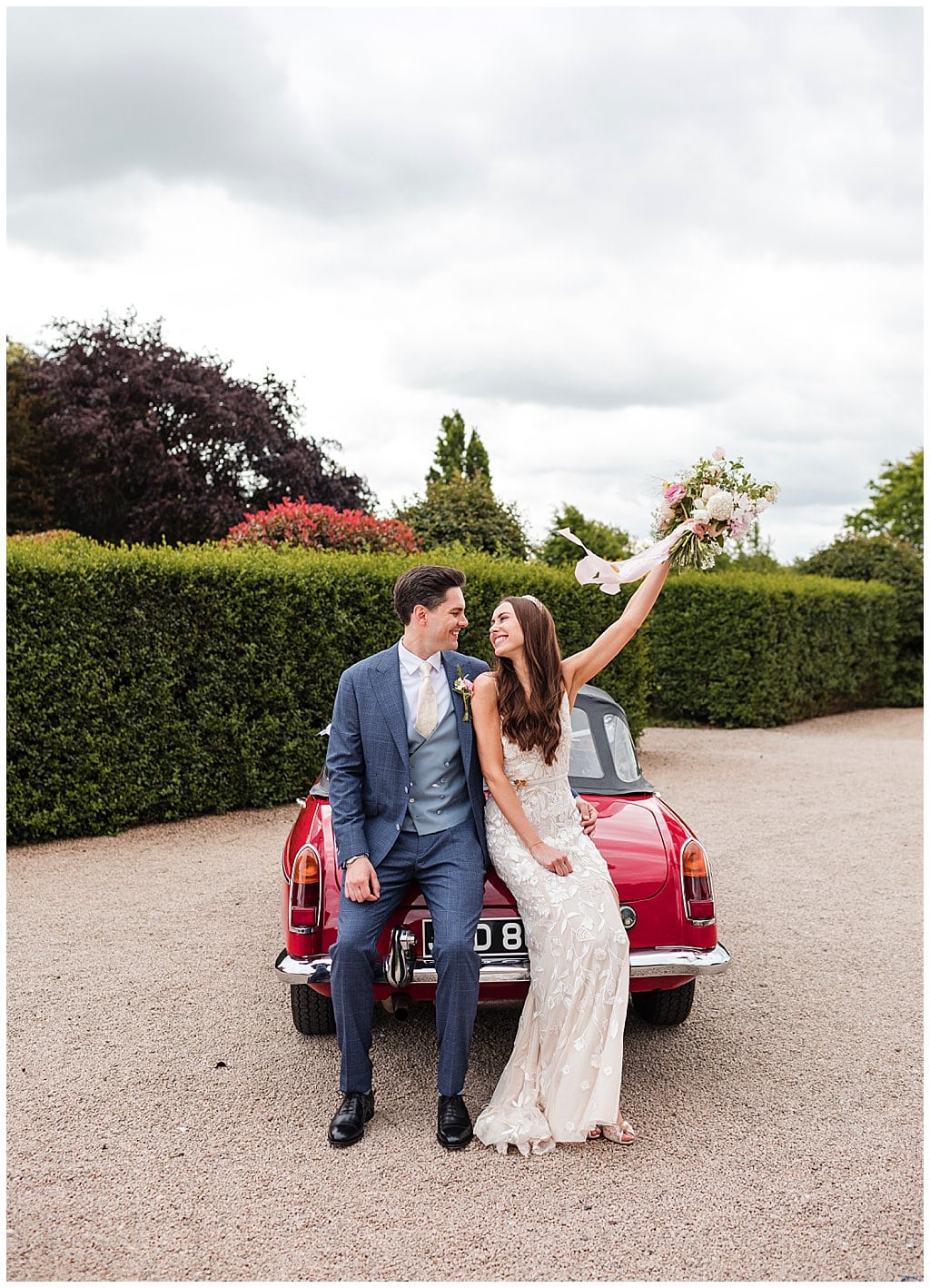 Bride and Groom looking at each other smiling, sitting on the back of a red sports car