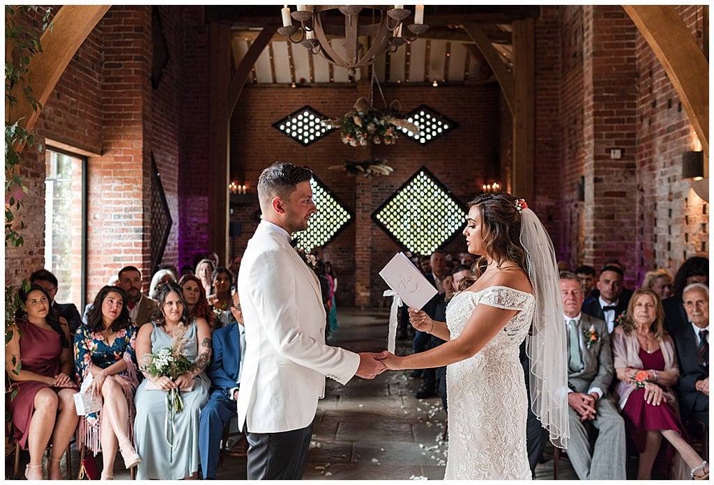 Bride and Groom hold hands and read personal vows to each other during their barn wedding ceremony