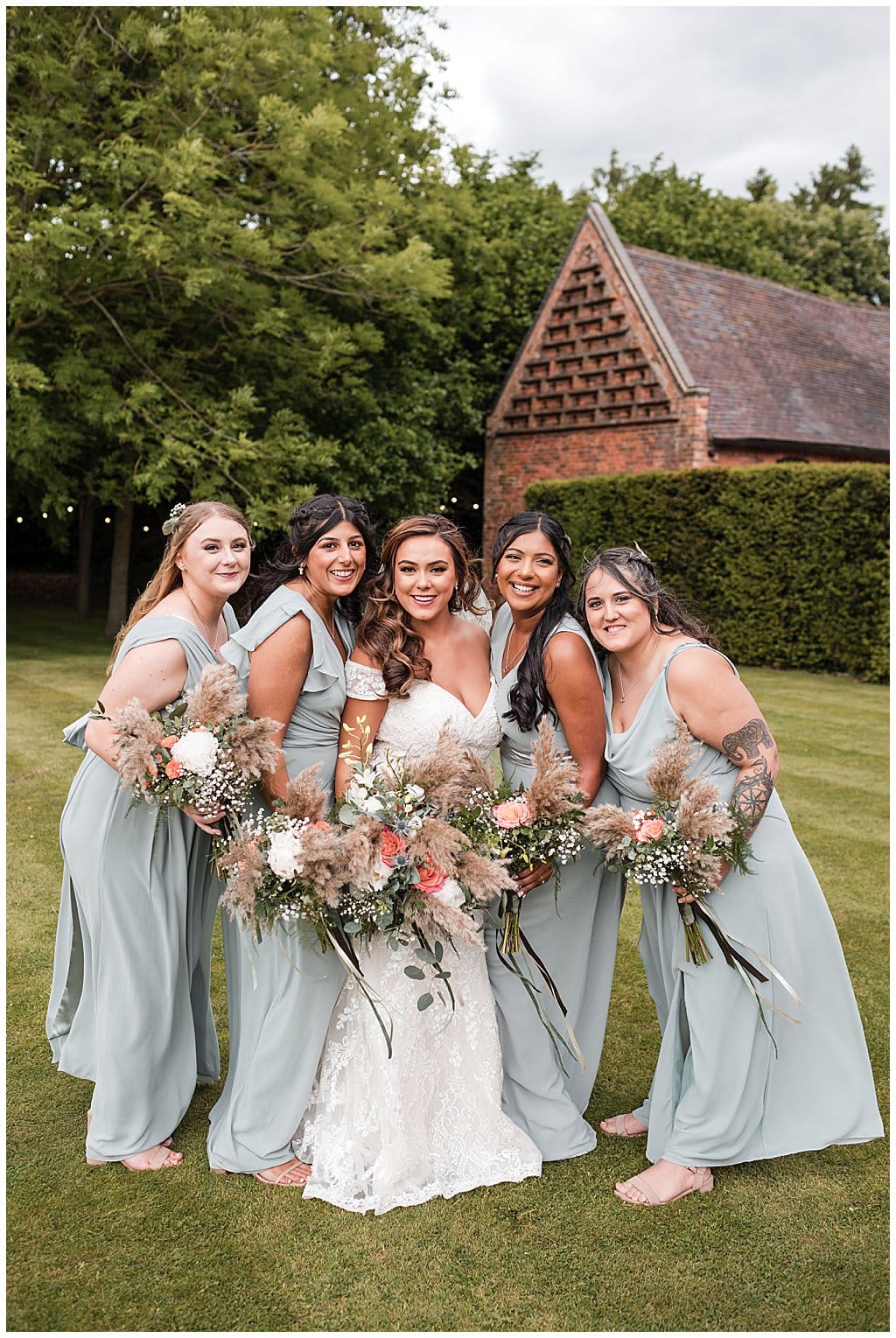Happy Bride with Bridesmaids wearing sage green, holding pampas bouquets outside Shustoke Barn