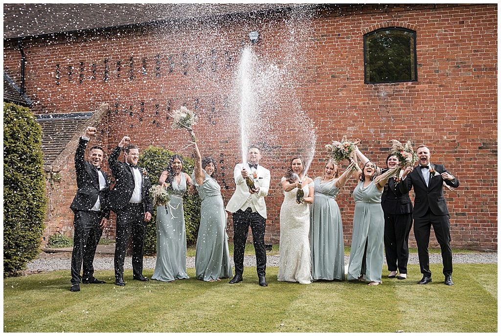 fun Bridal party spray champagne in front of Shustoke Barn. Prosecco spray photo