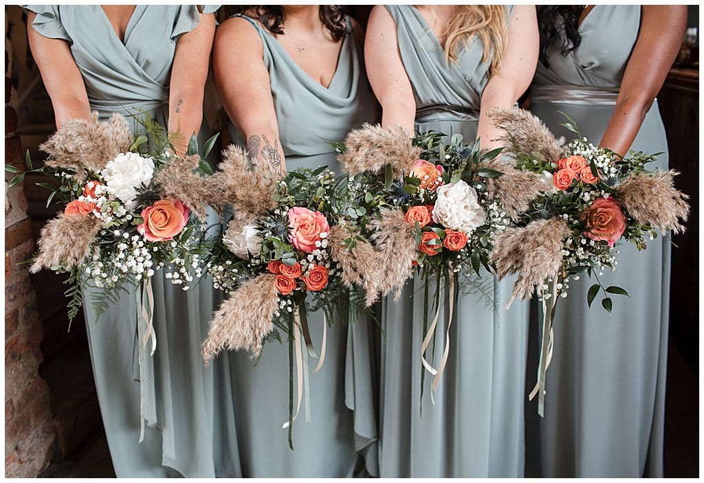 pampas and orange roses bouquets held by bridesmaids wearing sage green dresses