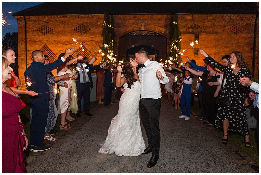Bride and Groom kissing in front of guests holding sparklers