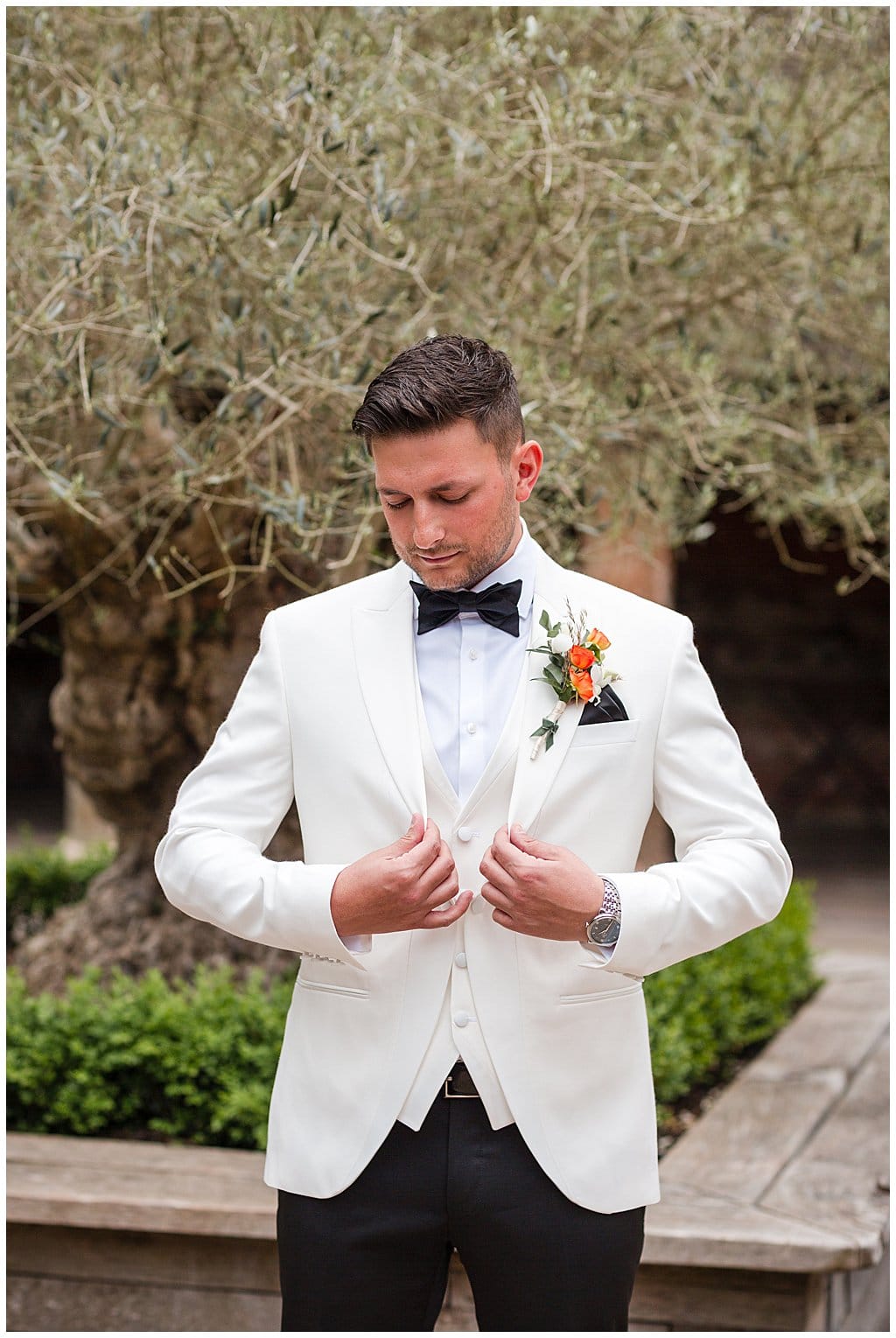 Groom wearing white tuxedo and black bow tie adjusting his jacket