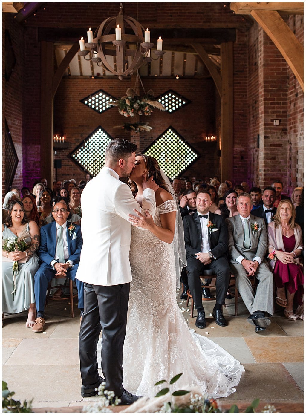 Just married Groom in white dinner jacket, kisses Bride. Happy guests cheering