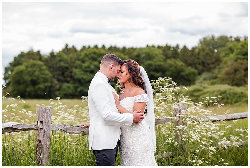 Romantic portrait of a Bride and Groom standing in front of white cow parsley flowers and rustic fence