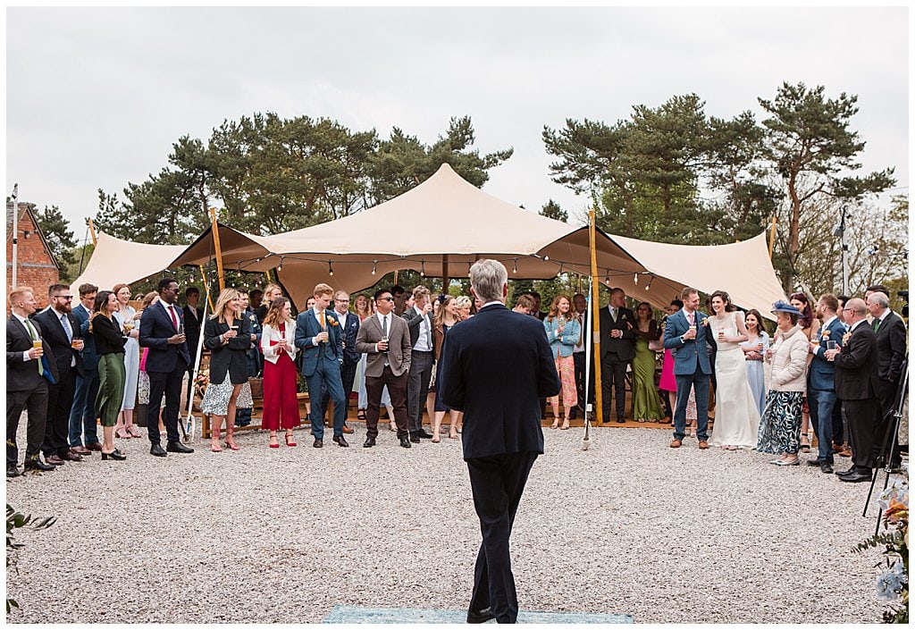 Father of the Bride gives wedding speech outside in front of a stretch tent and guests