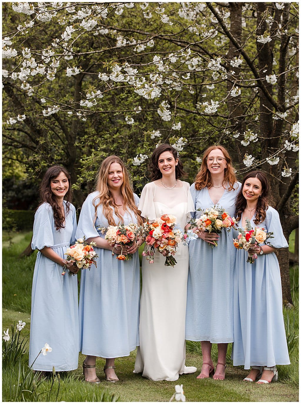 Bride and Bridesmaids with pretty spring bouquets stand in front of blossom trees in Pimhill Barn gardens