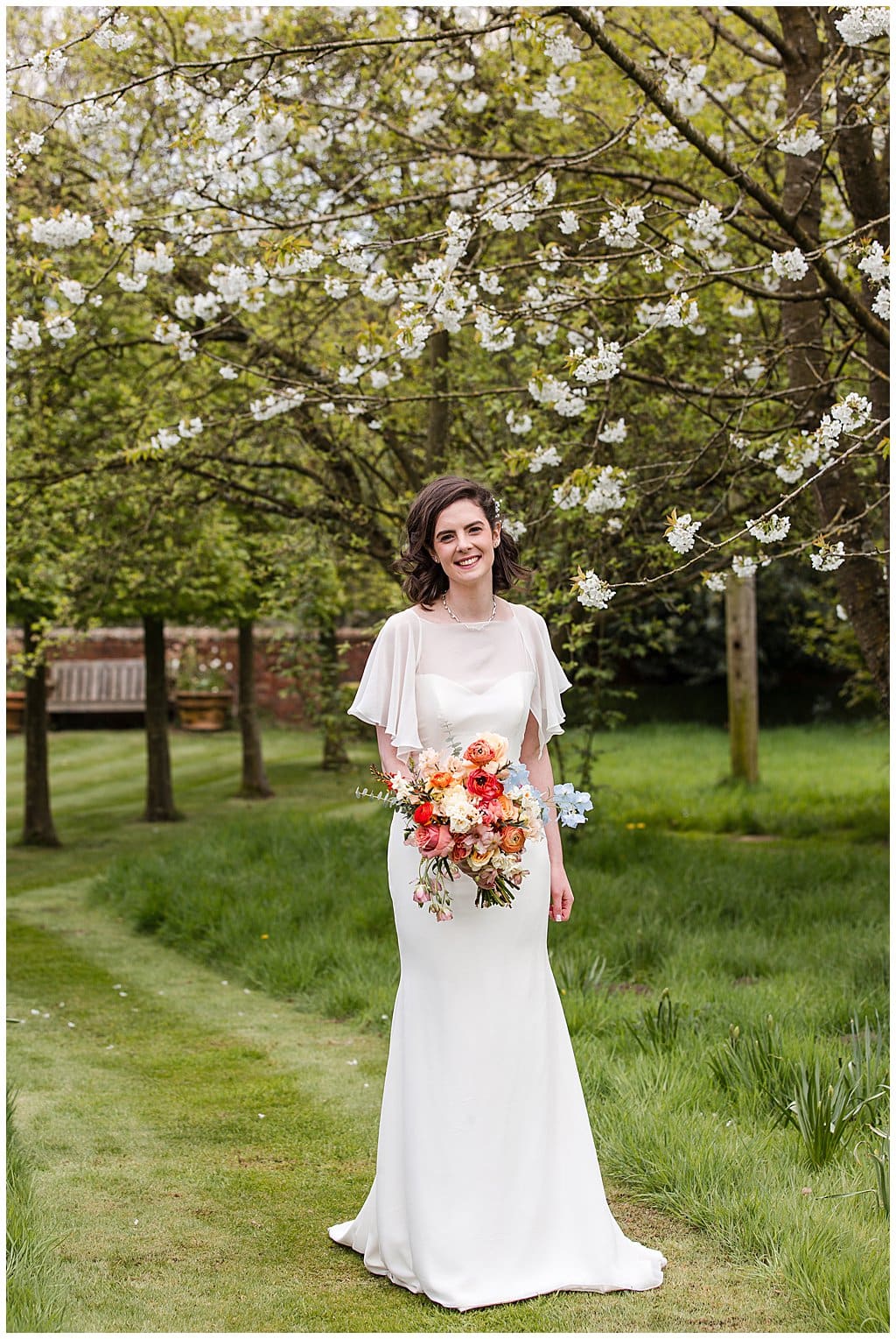 Happy Bride holding colourful Spring bouquet standing in the blossom orchard at Pimhill Barn