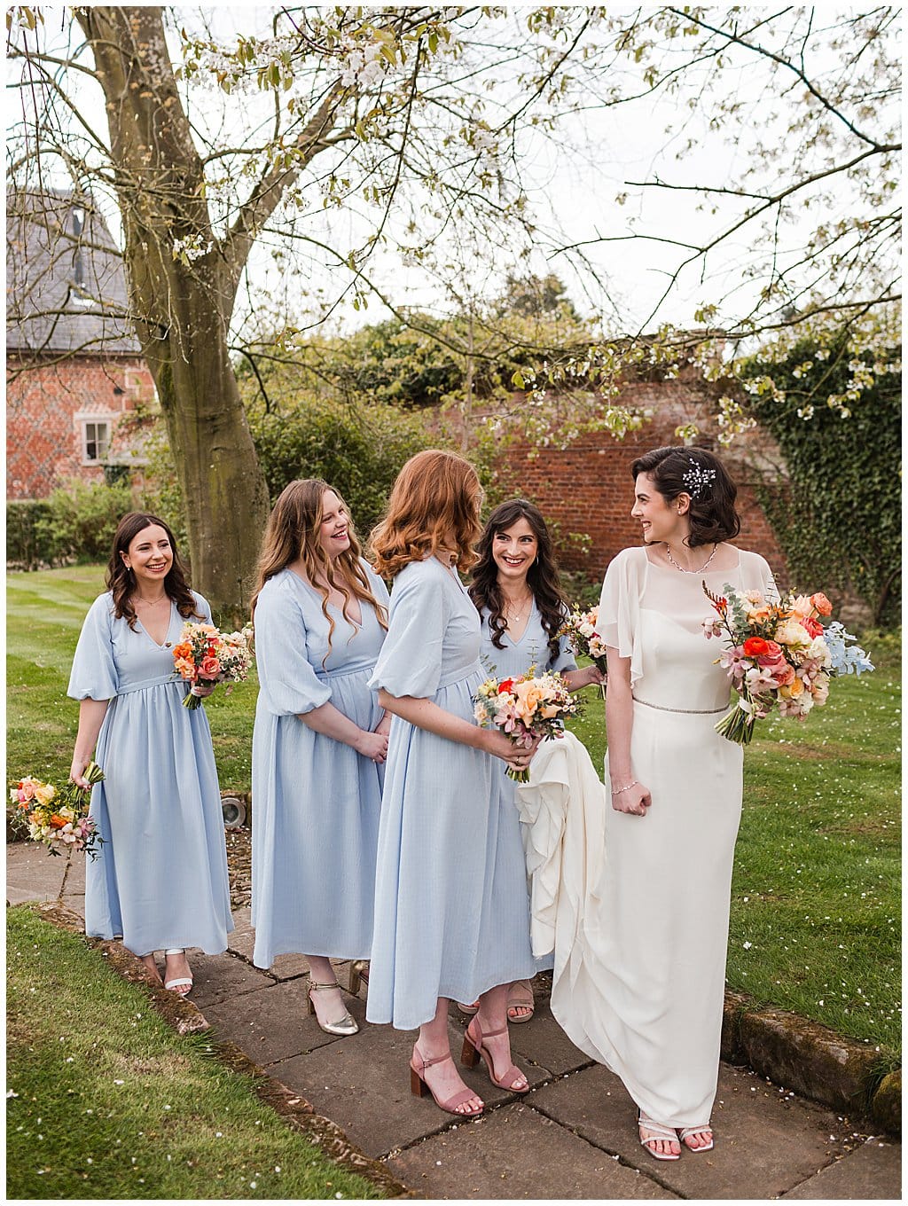 Bridesmaids wearing pale blue dresses, walking with the Bride in Spring gardens at Pimhill Barn