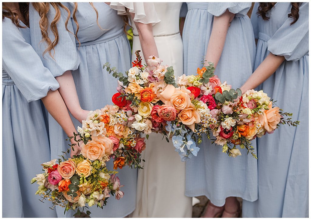 colourful wedding bouquets of Spring flowers, held against blue bridesmaid dresses