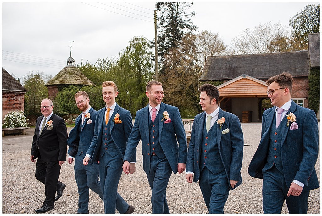 Groom and Groomsmen wearing blue tweed suits, chatting whilst walk in front of Pimhill Barn