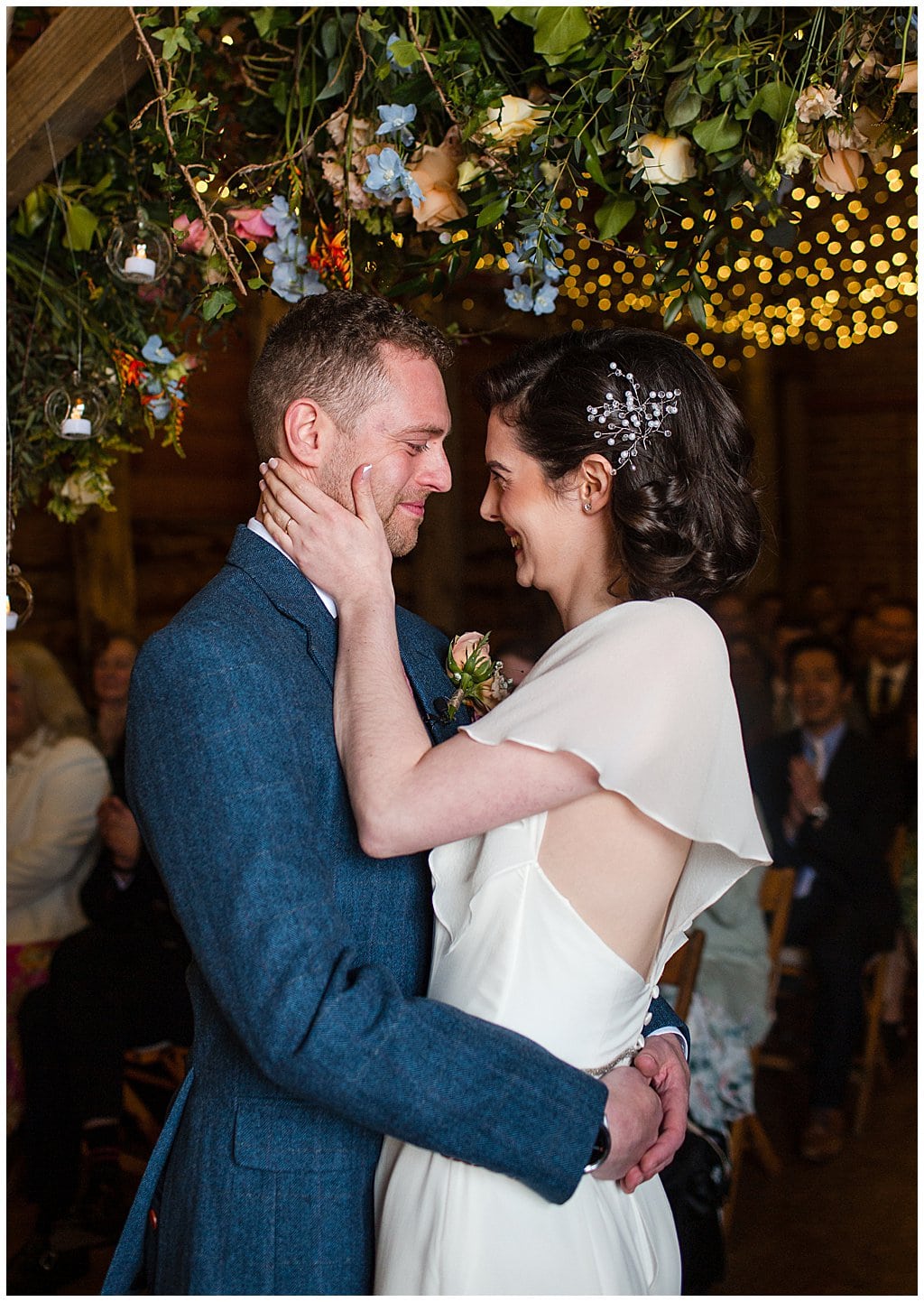 happy bride and groom hug standing under canopy of flowers and fairy lights in Pimhill Barn Shropshire