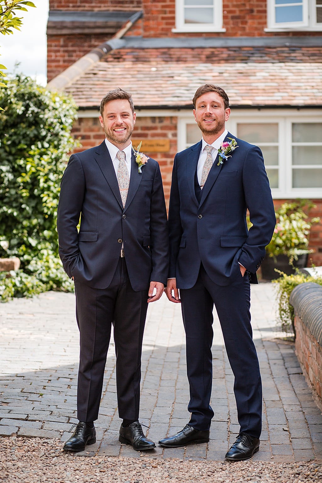Groom and Best Man wearing navy blue suits, stand in the courtyard at Curradine Barns