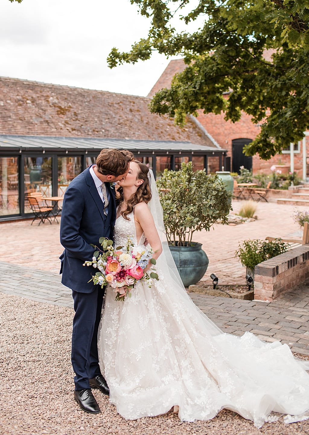 Bride and Groom stand kissing in the courtyard at Curradine Barns