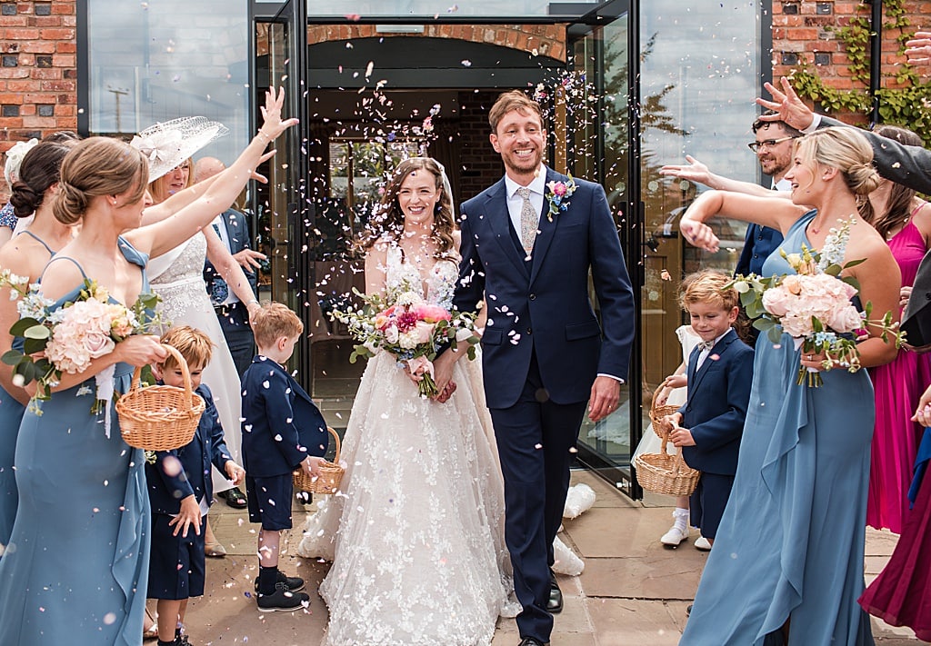 Happy smiling Bride and Groom walk out of the entrance of Curradine Barns to confetti 