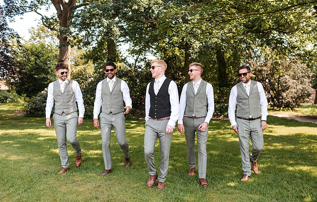 Groomsmen without jackets and wearing sunglasses walking and laughing together 
