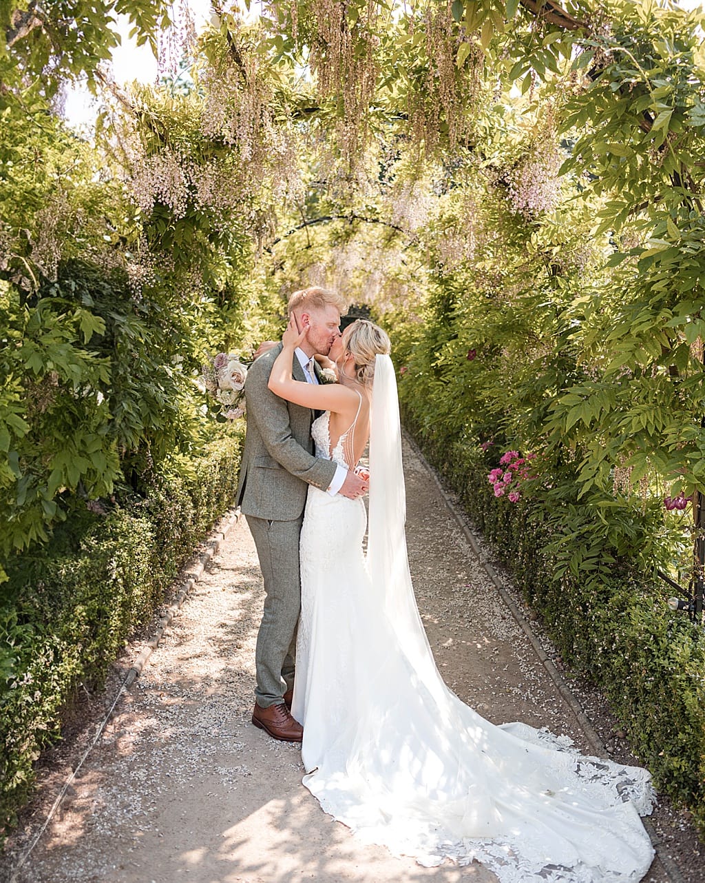 Bride and Groom kissing under an archway of Wisteria at Thorpe Garden