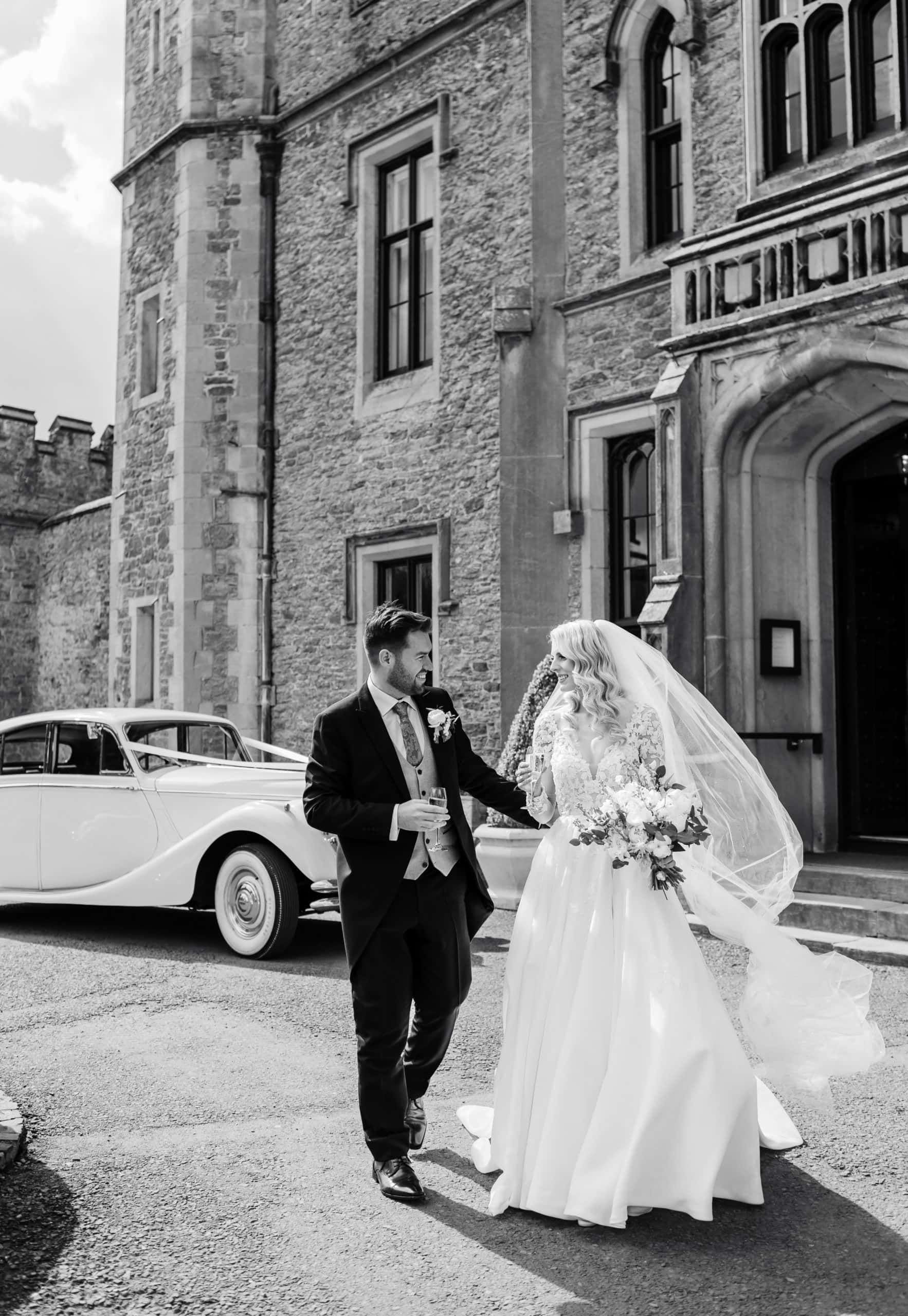 Bride and Groom walk at the front of Rowton Castle, holding drinks 