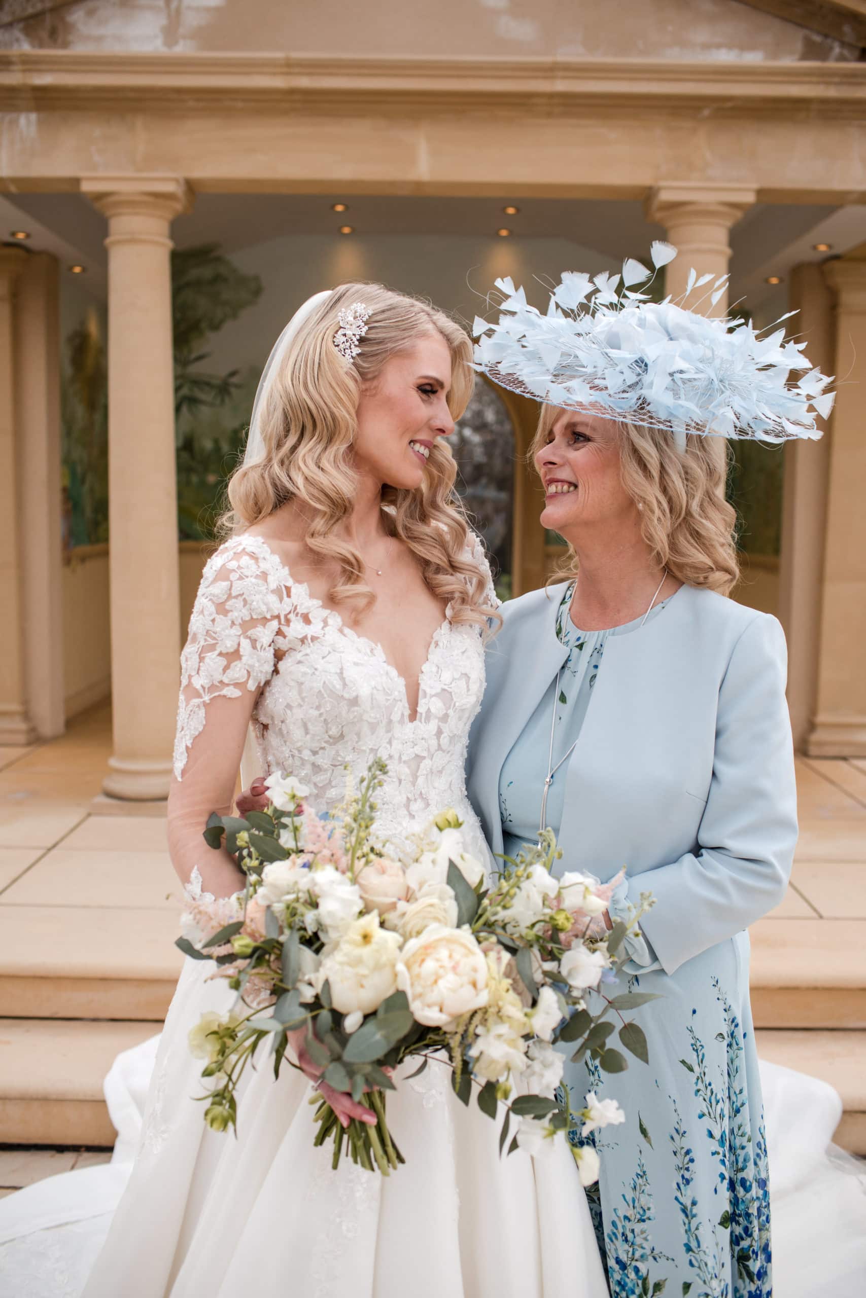 Bride and Mother of the Bride wearing pale blue two piece dress and jacket with pale blue hat