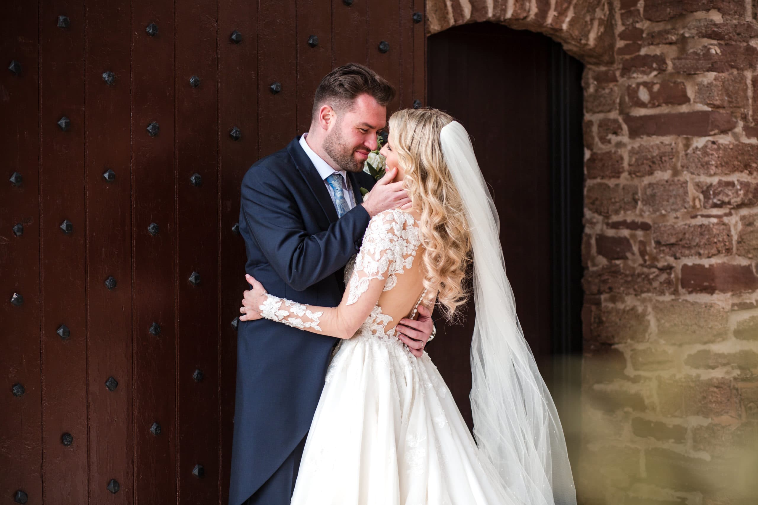 Bride wearing sheer back wedding dress with lace sleeves, shares an embrace with her new husband at Rowton Castle