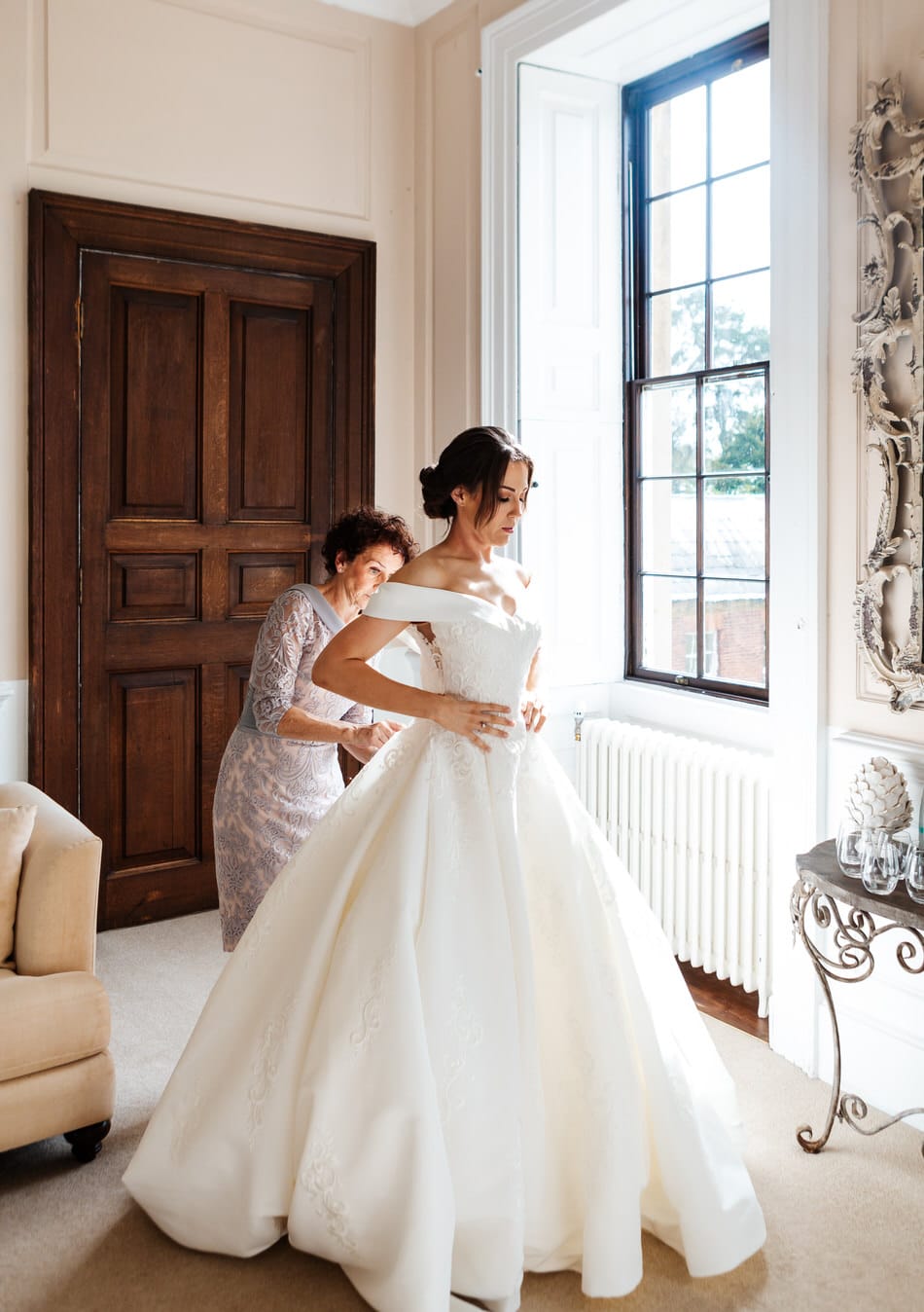 Mother of the Bride, helps the Bride button up her princess style wedding dress
