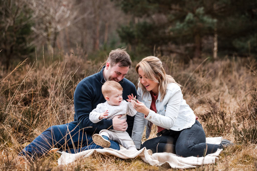 Parents sitting on a blanket with their toddler, exploring nature together during a natural, outdoor family photoshoot in Birmingham’s Sutton Park