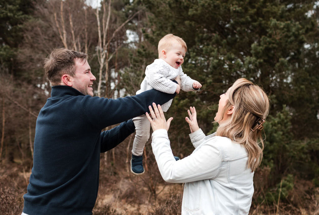 young parents lift their laughing toddler in the air during a family photoshoot in Sutton Par near Birmingham